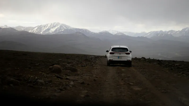 A car on the dirt road across the Deosai Plains, with snowy peaks behind