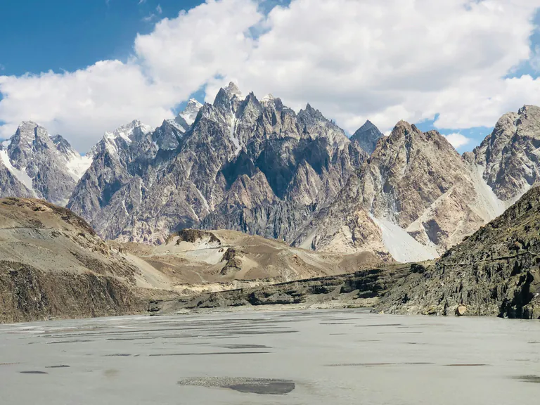 The jagged Passu Cones under white clouds, above the wide grey riverbed at Passu in upper Hunza