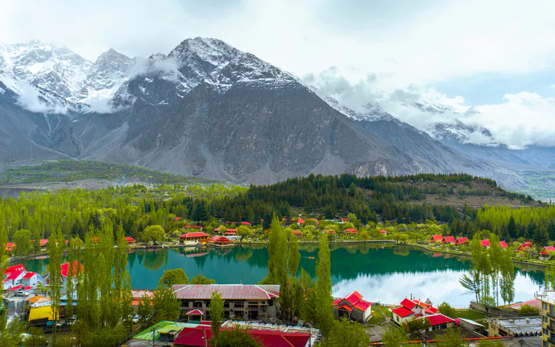 Red-roofed Shangrila resort reflected in a still lake below mountains in Skardu